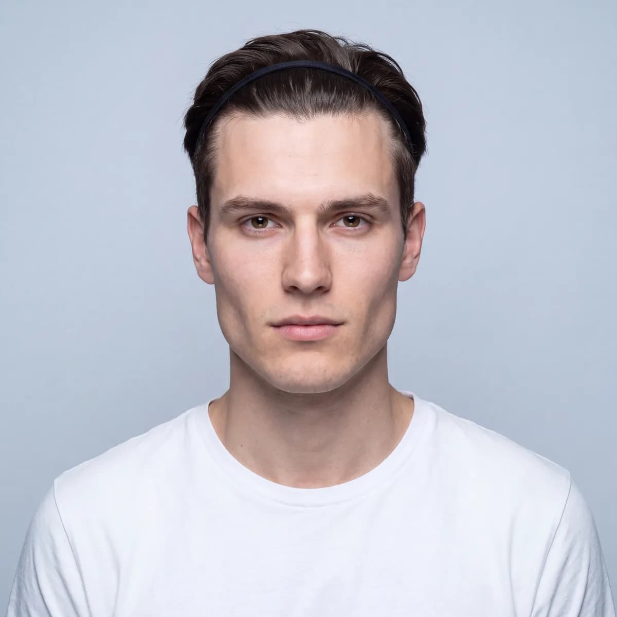 A correct front reference photo: square to the camera, pupils level, neutral expression, hair held off the forehead with a band, flat even light on a plain background.